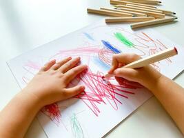 piccolo bambino disegna con colorato matite su carta su bianca tavolo. foto