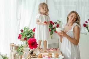 un' poco bionda ragazza con sua mamma su un' cucina controsoffitto decorato con peonie. il concetto di il relazione fra madre e figlia. primavera atmosfera. foto