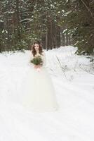 bellissimo sposa nel un' bianca vestito con un' mazzo nel un' innevato inverno foresta. ritratto di il sposa nel natura foto