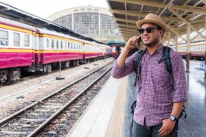 giovane uomo in piedi alla stazione ferroviaria e utilizza lo smartphone