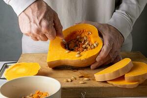 caucasico uomo è pulizia un' maturo zucca a partire dal semi nel il cucina. selettivo messa a fuoco. foto