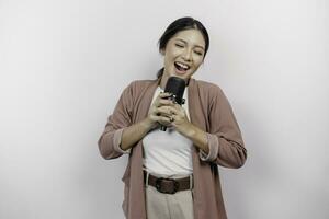 spensierato asiatico donna è avendo divertimento karaoke, cantando nel microfono mentre in piedi al di sopra di bianca sfondo foto
