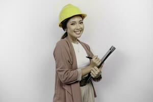 sorridente giovane asiatico donna dipendente indossare sicurezza casco mentre Tenere un' appunti, isolato di bianca sfondo foto