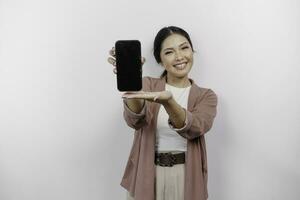 sorridente giovane asiatico donna dipendente indossare cardigan mentre mostrando copia spazio su sua Telefono schermo, isolato di bianca sfondo foto