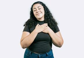 positivo latino ragazza con mani su il petto. grato giovane donna con mani su il petto. grato adolescenziale ragazza sorridente con mani su il petto isolato foto