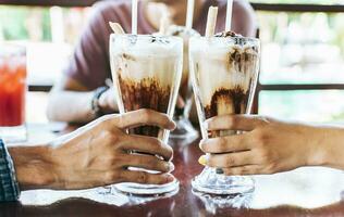 uomo e donna mano tostatura e Tenere Due frappè. Due mani tostatura con frappè nel un' bar, vicino su di Due mani tostatura con ghiacciato caffè nel un' bar. foto