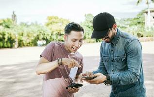 Due contento amici guardare a un' cellula Telefono nel il strada, Due sorridente amici guardare a media su il cellula Telefono nel il strada, Due giovane amici avendo divertimento con il cellula Telefono all'aperto foto