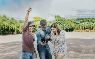 tre allegro persone guardare a cellula Telefono all'aperto, eccitato adolescenziale amici guardare a cellula Telefono schermo su il strada. tre eccitato amici guardare a il cellula Telefono nel il strada foto