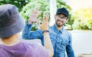 indietro Visualizza di Due sorridente amici tremante mani su il strada. Due sorridente amici tremante mani nel un' parco. concetto di Due amici saluto ogni altro con un' stretta di mano su il strada. foto