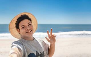 contento giovane uomo assunzione un' autoscatto su il spiaggia. vicino su di tipo nel cappello assunzione un' autoscatto su spiaggia vacanza. sorridente uomo assunzione un' autoscatto su vacanza con pollice su foto