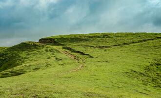 un' collina circondato di altro verde colline, un' sentiero per un' verde collina con blu cielo con copia spazio foto