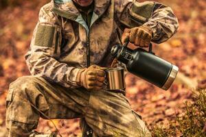 cacciatore riscaldamento su di potabile un' caffè a partire dal il suo thermos foto