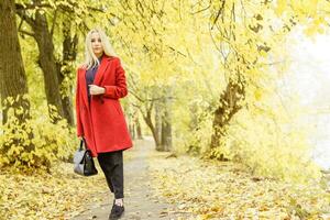 un' giovane bionda donna passeggiate in giro il autunno città nel un' rosso cappotto. il concetto di urbano stile e stile di vita foto