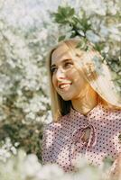 bionda ragazza su un' primavera camminare nel il giardino con ciliegia fiori. femmina ritratto, avvicinamento. un' ragazza nel un' rosa polka punto vestire. foto