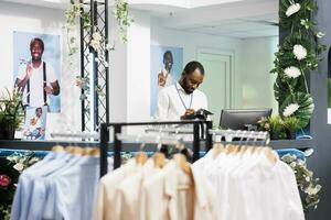 capi di abbigliamento memorizzare africano americano dipendente Lavorando a contatore, pianificazione i saldi e scrittura nel organizzatore. shopping centro commerciale moda Dipartimento assistente in piedi a check-out scrivania foto