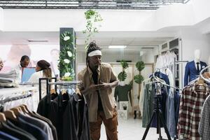 africano americano influencer registrazione promozionale video per capi di abbigliamento marca utilizzando smartphone su tripode nel moda boutique. blogger pubblicità abbigliamento maschile su sociale media per seguaci foto