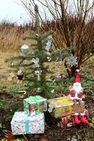 foto di un' giocattolo gnomo seduta su i regali vicino un' vivere decorato Natale albero all'aperto nel il cortile, generale Piano
