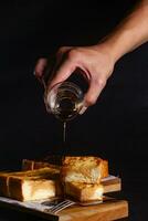 miele scrosciante a partire dal un' cucchiaio in un' bicchiere di bianca pane su nero sfondo foto