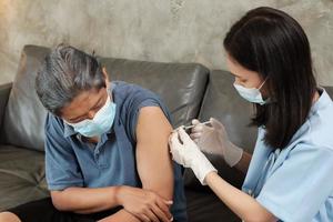una dottoressa asiatica sta vaccinando un uomo anziano a casa.