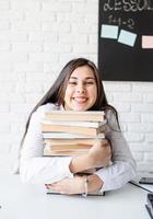 giovane insegnante seduto con una pila di libri che guarda lontano pronto per la lezione foto