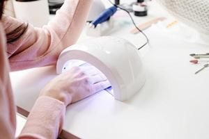 donna nel salone di manicure che si asciuga le unghie in una lampada uv foto