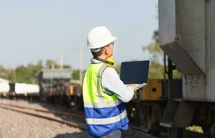 ingegnere sotto ispezione e controllo costruzione processi ferrovia locomotiva riparazione pianta, ingegnere uomo nel gilet e elmetti e con il computer portatile nel un' ferrovia deposito foto