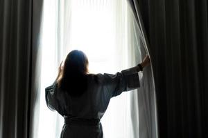 la bella donna sta aprendo la tenda alla finestra al mattino foto
