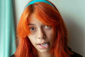 divertente adolescente ragazza con rosso capelli Spettacoli blu lingua. il ragazza è Ingannare in giro foto