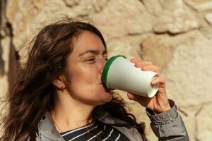 un' di mezza età donna bevande caffè a partire dal un' carta tazza al di fuori su un' soleggiato autunno giorno foto