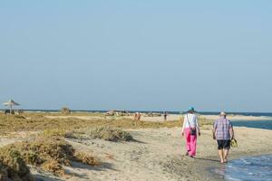lotto di persone a piedi nel il sabbia su il spiaggia vicino il mare durante vacanza nel il primavera foto