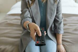 vicino su televisione a distanza controllo nel mano donna puntamento per tv impostato e svolta esso su o spento. Selezionare canale Guardando tv a casa nel il vivente camera relax. foto