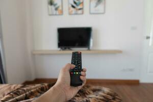 vicino su televisione a distanza controllo nel mano uomo puntamento per tv impostato e svolta esso su o spento. Selezionare canale Guardando tv a casa nel il vivente camera relax. foto