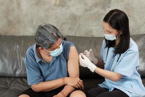 una dottoressa asiatica sta vaccinando un uomo anziano a casa.