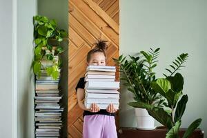 un' ragazza detiene un' grande pila di libri contro il sfondo di un' casa. foto