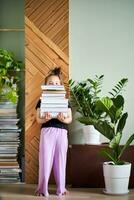 un' ragazza detiene un' grande pila di libri contro il sfondo di un' casa. foto