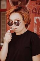 ragazza con capelli corti rossi e occhiali da sole a specchio che fuma sigaretta