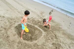 bambini scavare un' buco nel il sabbia su il spiaggia. foto