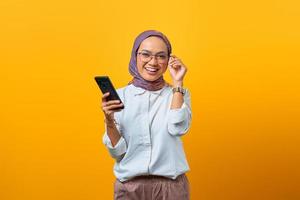 donna asiatica sorridente che tocca gli occhiali e tiene il cellulare foto