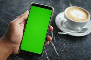 tenendo una cpu di caffè e utilizzando uno smartphone con schermo verde foto