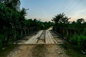 un' di legno ponte al di sopra di un' sporco strada nel il mezzo di il foresta foto