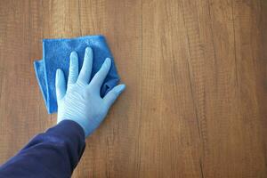 mano in guanti di gomma blu che puliscono il tavolo con un panno foto