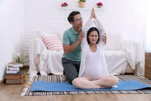 marito prendere cura il suo moglie incinta Aiuto esercizio di yoga nel vivente camera a casa. gravidanza coppia assistenza sanitaria e relazione concetto. foto