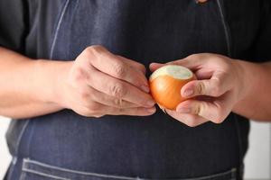 le mani dello chef che sbucciano una cipolla per cucinare la zuppa foto