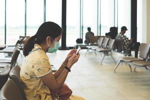 giovane donna asiatica seduta in aeroporto e con indosso la maschera facciale foto