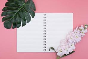 diario bianco con fiori e foglie verdi su sfondo rosa foto