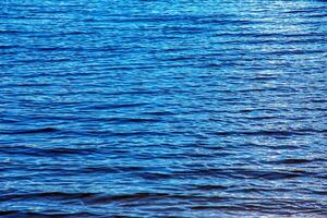 acqua ondulazione struttura sfondo. ondulato acqua superficie durante tramonto, d'oro leggero riflettendo nel il acqua. foto