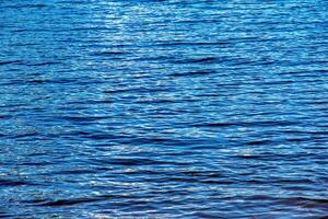 acqua ondulazione struttura sfondo. ondulato acqua superficie durante tramonto, d'oro leggero riflettendo nel il acqua. foto