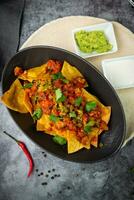 nachos con salsa, carne e erbe aromatiche nel un' nero piatto, superiore Visualizza foto