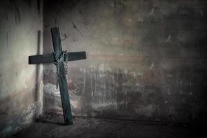 croce nera contro il muro con catena d'acciaio appesa e pistola