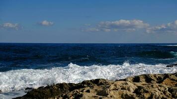 blu mare onda e bianca schiuma e spruzzata. pietra spiaggia su isola di Malta, no sabbioso spiaggia. estate vacanza confine telaio concetto. tropicale isola vacanza sfondo. turista viaggio bandiera design modello. foto